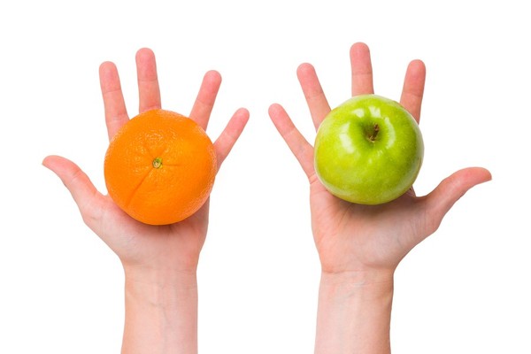Left hand holding an orange in the palm, and right hand holding a green apple.