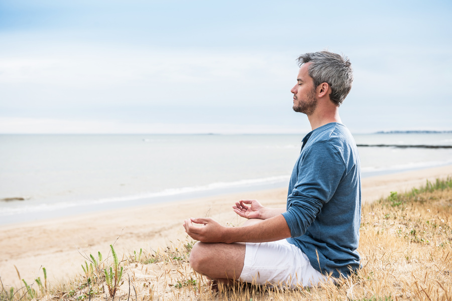 Man sitting on a beach in a meditative pose.