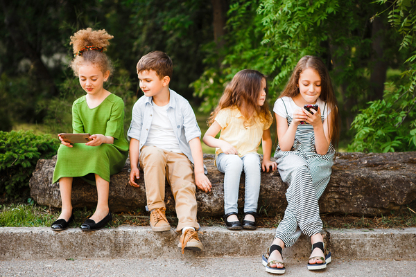 Group of young teens sitting outside looking at their phones.
