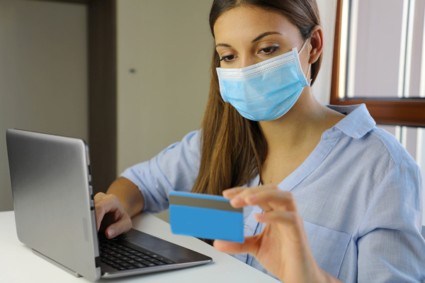 Woman wearing a protective face mask while typing on a computer and holding a credit card.
