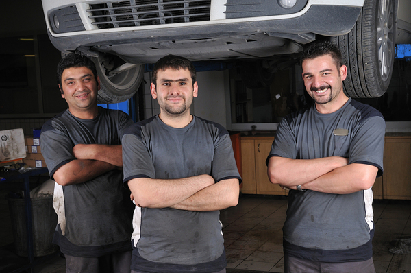 Three men smiling while crossing their arms near a car on a lift.