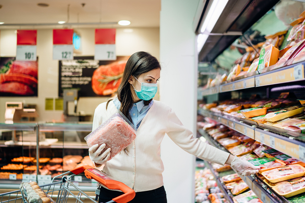 Woman shopping in a grocery store using a face mask and gloves.